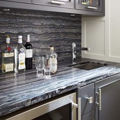 a marble counter top in a kitchen with wine glasses and liquor bottles on the counter