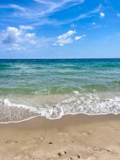 the beach has waves coming in from the ocean and blue sky with white clouds above