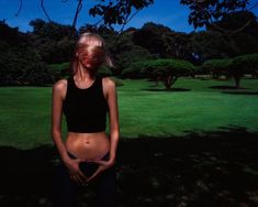 a woman standing in the grass with her back to the camera, holding her belly