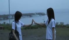 two girls standing in front of a body of water with their hands up to each other