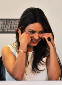 a woman smiles as she holds her hand up to her face while sitting in front of a microphone