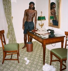 a man standing in front of a mirror next to a desk with a lamp on it