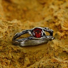 a silver ring with a red stone in the middle on some rocks and dirt surface