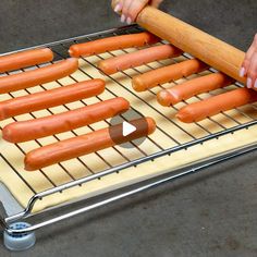 a person is rolling up hot dogs on a grill