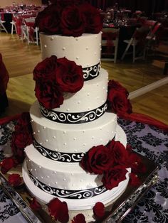 a three tiered wedding cake with red roses on the top and black trimmings