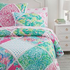 a bed with pink, green and blue comforter in a bedroom next to a white dresser