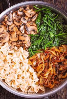 a pan filled with pasta, mushrooms and spinach on top of a wooden table