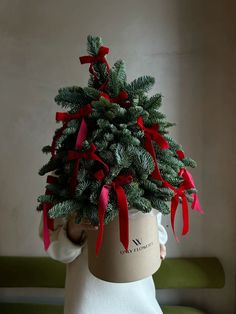 a small christmas tree in a pot with red bows on it's head and hands