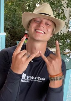 a young man wearing a hat making the peace sign with his hands while sitting at a table