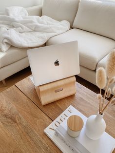 an apple laptop sitting on top of a wooden table next to a vase with dry grass in it