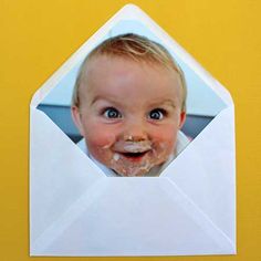 a baby with food in it's mouth is looking through an envelope to the camera