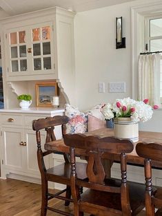 a kitchen with white cabinets and wooden chairs in front of a table filled with flowers