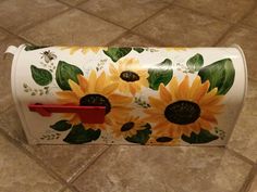 a white mailbox with sunflowers painted on the front and sides, sitting on a tile floor