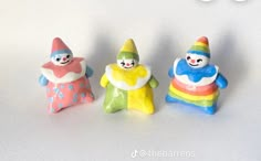 three small toy snowmen standing next to each other on a white surface with one wearing a rainbow colored hat