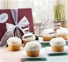 four cupcakes with white frosting on them sitting in front of a gift box