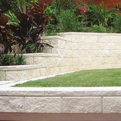 a wooden bench sitting in the middle of a lush green park next to a stone wall