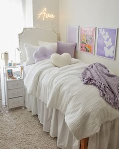 a white bed sitting in a bedroom next to a night stand with two pictures on the wall