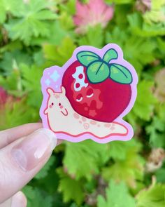 a hand holding up a sticker with an apple on it's side in front of green leaves