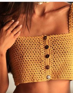 a woman wearing a yellow crochet crop top with buttons on the front and bottom