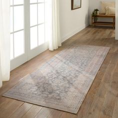 a living room with hardwood floors and white curtains on the windowsill, along with a large rug