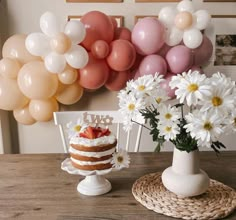 there is a cake and flowers on the table with balloons in the backround