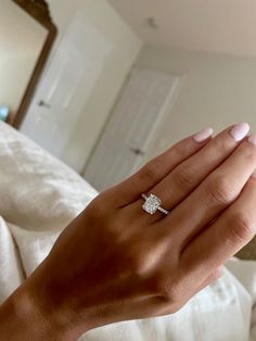 a woman's hand with a diamond ring on top of her finger, in front of a bed