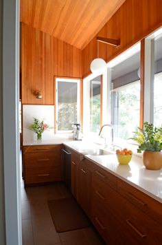 a kitchen with wood paneling and white counter tops, along with a bowl of fruit on the counter