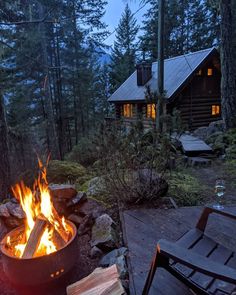 a fire pit sitting in the middle of a forest next to a wooden table and chairs