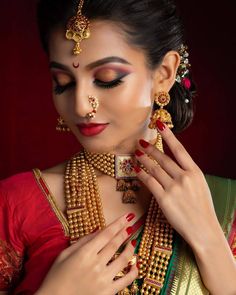 a woman wearing gold jewelry with red and green accents on her face, holding onto the necklace