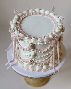 there is a wedding cake on top of a stand with ribbon around the edges and seashells