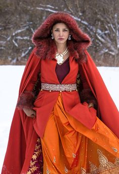 a woman in an orange and red outfit with fur on her head is walking through the snow