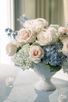 a vase filled with white and blue flowers sitting on top of a table next to candles