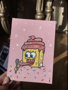 a hand holding up a pink card with an image of a cupcake on it