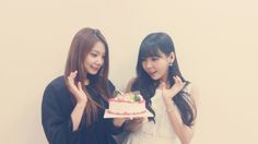 two young women standing next to each other with a cake in front of their faces