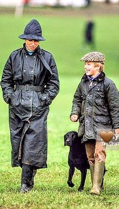 two people and a dog are walking in the grass with one person wearing a raincoat