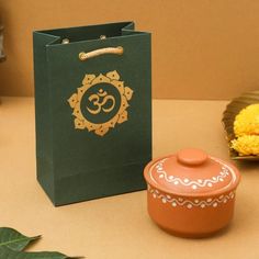 a small tea pot next to a green bag with an omesh symbol on it