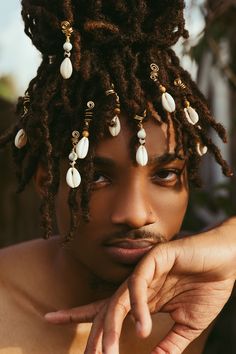 a young man with dreadlocks and pearls on his hair looks at the camera