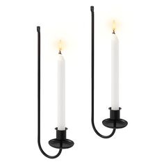 two white candles are hanging on the wall with black metal brackets and one is lit