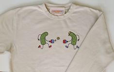 Independent Trading Co beige sweatshirt with two cartoon applique pickles playing pickleball. The design measures approximately 10x4 inches and is machine embroidered. Pickleball Painting, Pickleball Shirts Funny, Cool Shirts Aesthetic, Pickle Shirt, Pickleball Sweatshirt, Pickleball Outfit, Playing Pickleball, Quilt Size Chart, Beige Sweatshirt