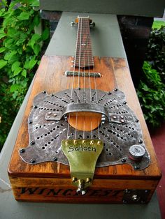 an old guitar is sitting on top of a wooden box in front of some bushes