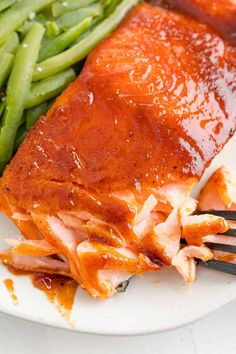 a white plate topped with green beans and meat covered in sauce next to a fork