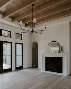 an empty living room with white walls and wood floors, large windows on either side of the fireplace