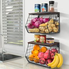 two metal baskets filled with fruit on top of a white counter next to a window