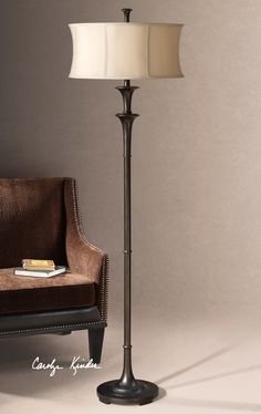 a lamp that is next to a chair and a book on a table in front of a gray wall