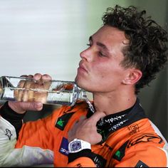 a man drinking from a glass bottle while wearing an orange and white uniform with his hands on his chest