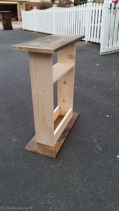 a wooden table sitting on top of a parking lot next to a white picket fence