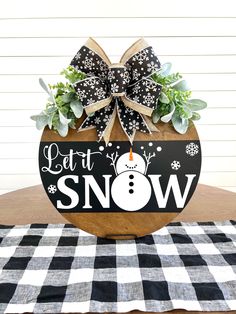 a wooden sign that says let it snow on top of a table with a black and white checkered cloth