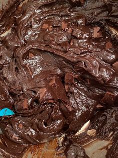 a wooden bowl filled with chocolate frosting on top of a table next to a blue spatula