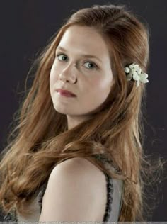 a woman with long red hair wearing a flower in her hair and looking off to the side