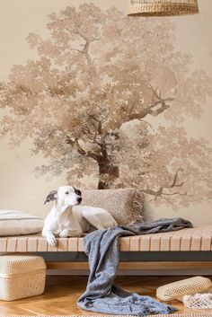 a white dog sitting on top of a bed next to a wall with a tree painted on it